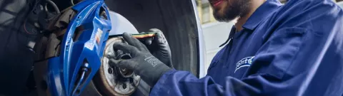 A Point S technician measuring brake pad thickness on a car during a brake check