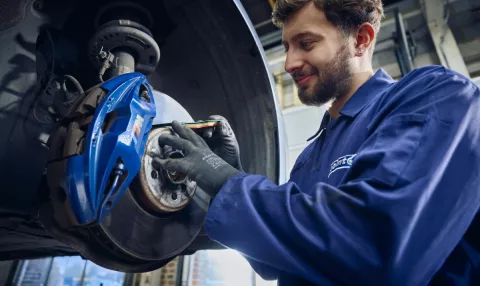 A Point S technician measuring brake pad thickness on a car during a brake check