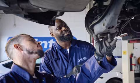 Two Point S technicians inspecting a worn shock absorber on a car