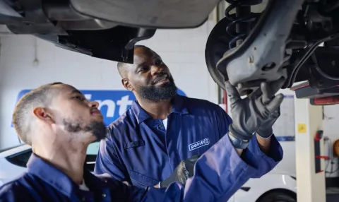 Two Point S technicians inspecting a worn shock absorber on a car