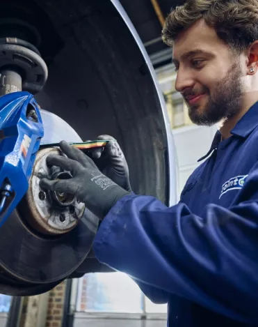 A Point S technician measuring brake pad thickness on a car during a brake check