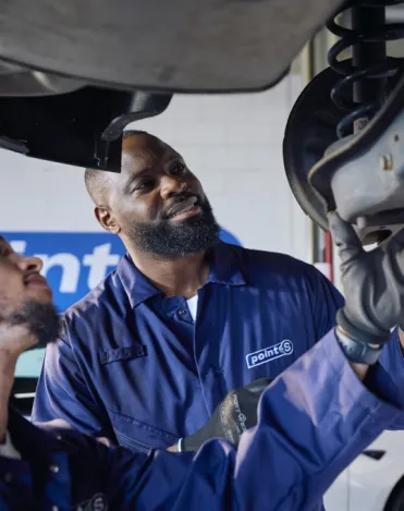 Two Point S technicians inspecting a worn shock absorber on a car